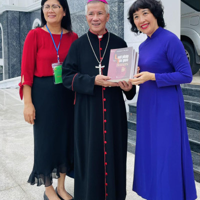 IGE Program Manager Hien Vu (left) and Director of Ho Chi Minh National Academy of Politics' Institute of Religion and Belief Madame Do Lan Hien (right) presents a book on "Religion and Rule of Law" to Vietnamese Catholic Bishop Alphonse Huu Long Nguyên (center).