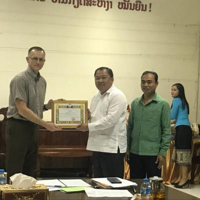 Mr. Khanonglith, director of the Department of Religious Affairs at the Lao Front for National Development, presents Dr. Bailey with his official commendation.  